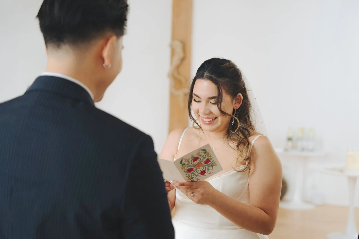 A bride reading a card or letter from the groom during their wedding ceremony, smiling happily.