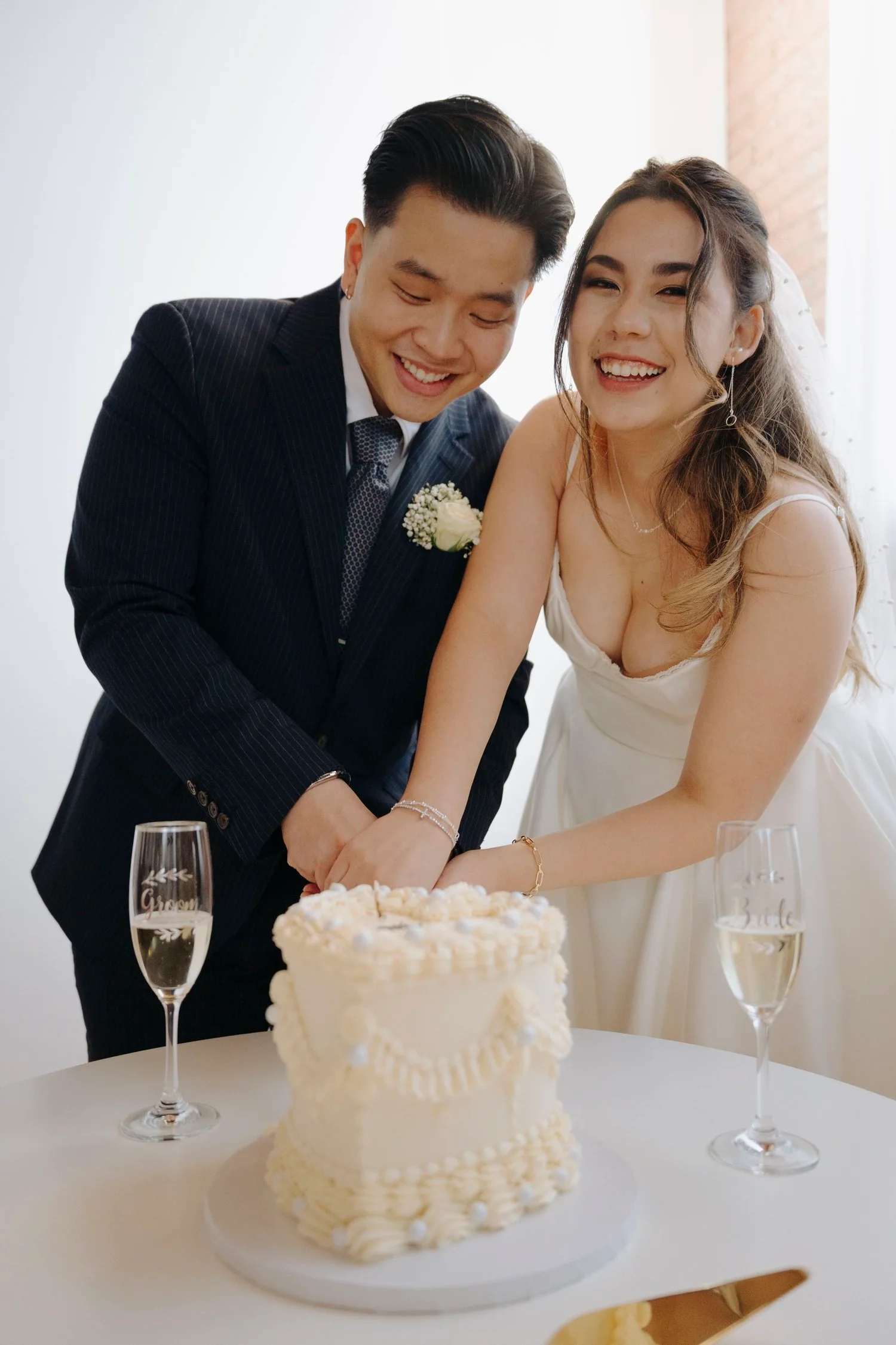 A newly married couple in wedding attire cutting a wedding cake together, smiling joyfully.